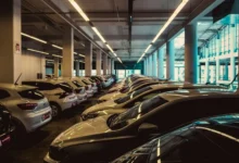 Rzędy zaparkowanych samochodów w wielopoziomowym parkingu, długie świetlówki pod betonowym sufitem