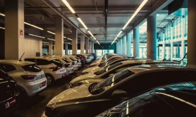 Rzędy zaparkowanych samochodów w wielopoziomowym parkingu, długie świetlówki pod betonowym sufitem