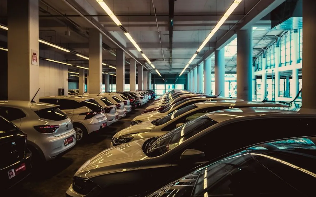 Rzędy zaparkowanych samochodów w wielopoziomowym parkingu, długie świetlówki pod betonowym sufitem
