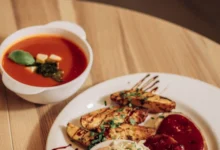 Zupa pomidorowa z bazylią i talerz pieczonych ćwiartek ziemniaków z surówką na drewnianym stole